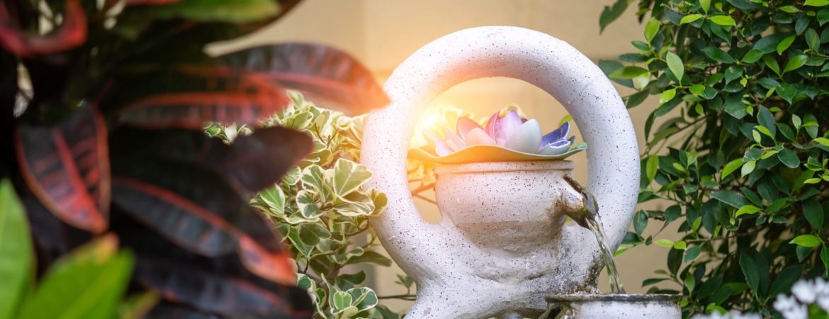 A serene garden fountain featuring a beautiful lotus flower, surrounded by vibrant greenery and sunlight, creating a peaceful outdoor atmosphere.