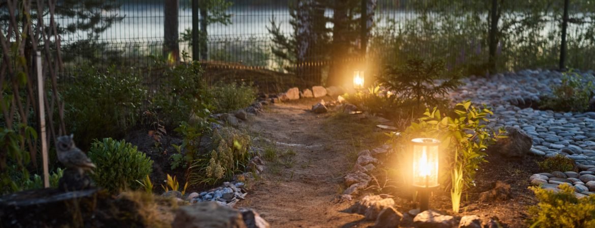 A serene garden path lit by soft lanterns, surrounded by lush greenery, creating a peaceful dusk atmosphere