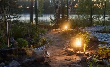 A serene garden path lit by soft lanterns, surrounded by lush greenery, creating a peaceful dusk atmosphere