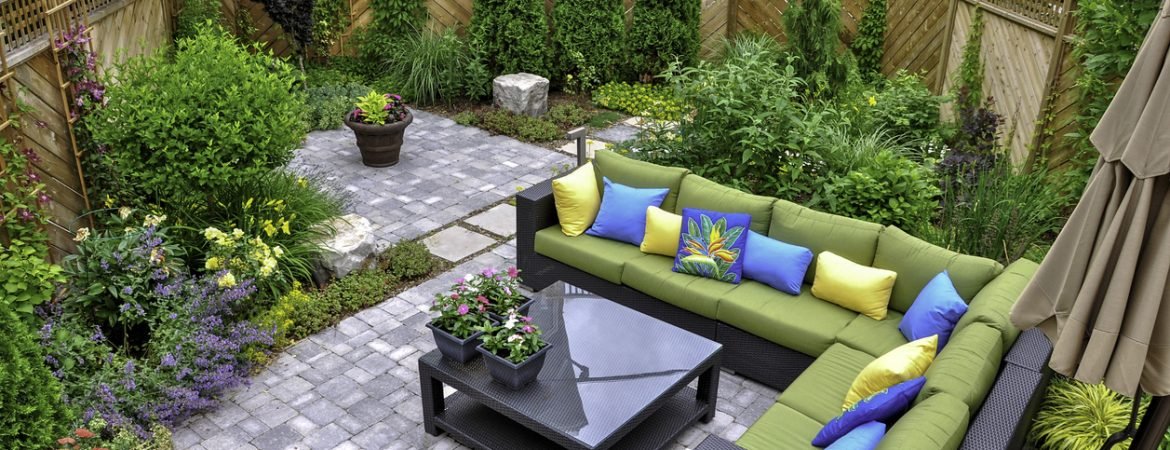 A beautiful small, urban backyard garden featuring a tumbled paver patio, flagstone stepping stones, and a variety of trees, shrubs and perennials add colour and year round interest.